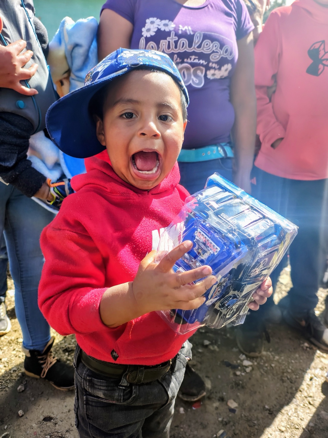 Niño sonriente con sudadera roja y gorra azul sosteniendo un regalo